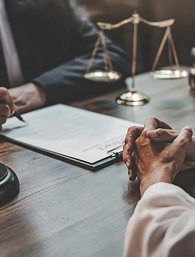 a lawyer or judge wearing a suit sits at a desk with a document, scales of justice in the background, and a gavel nearby.