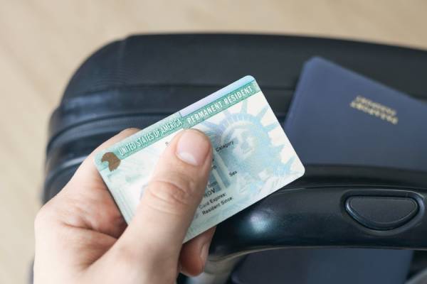 Man holding permanent resident (green) card. United States passport on suitcase. Application to register permanent residence.